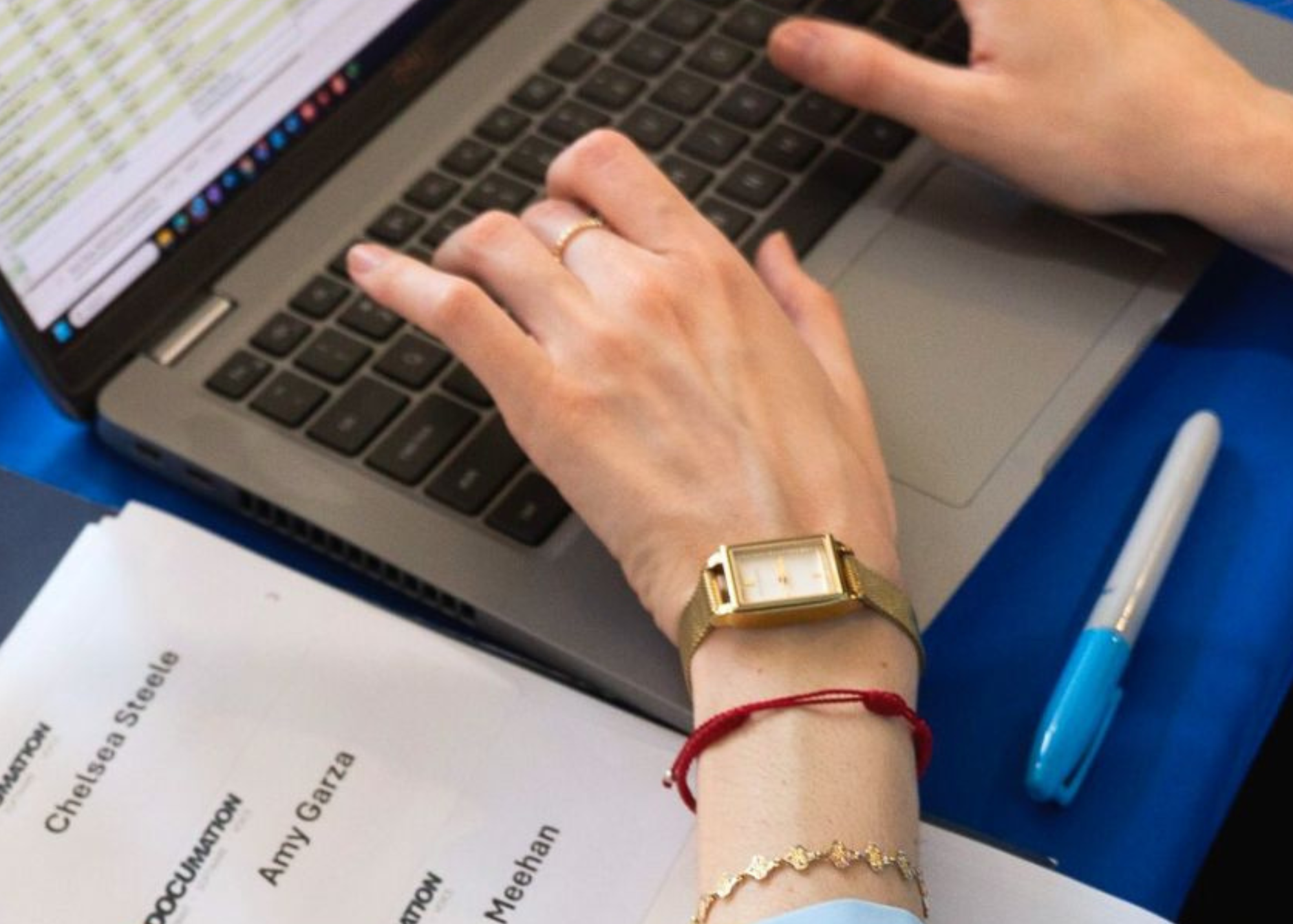 Hands typing on a laptop keyboard beside printed documents and a pen on a desk.