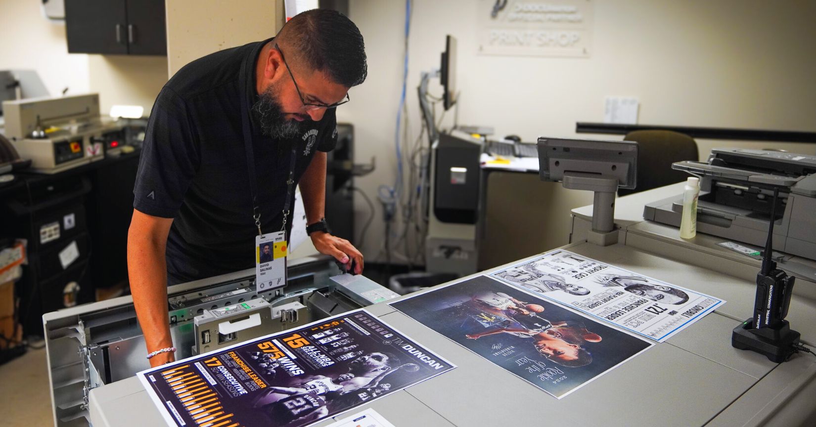 A print specialist reviews high-quality sports posters as they come off a large-format printer in a professional print shop.