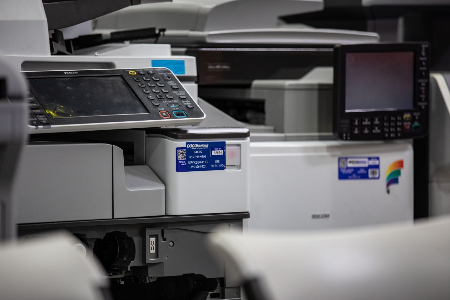 Close-up of Ricoh multifunction printers with DOCUmation service labels in an office setting.