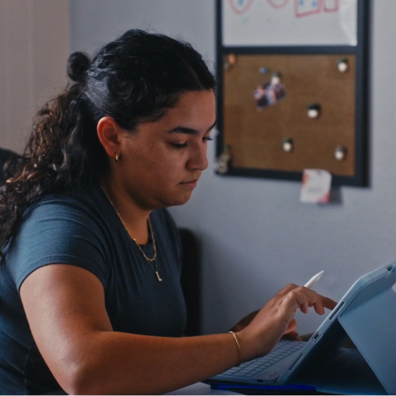 A young woman works on a tablet with a stylus in a home office setting.