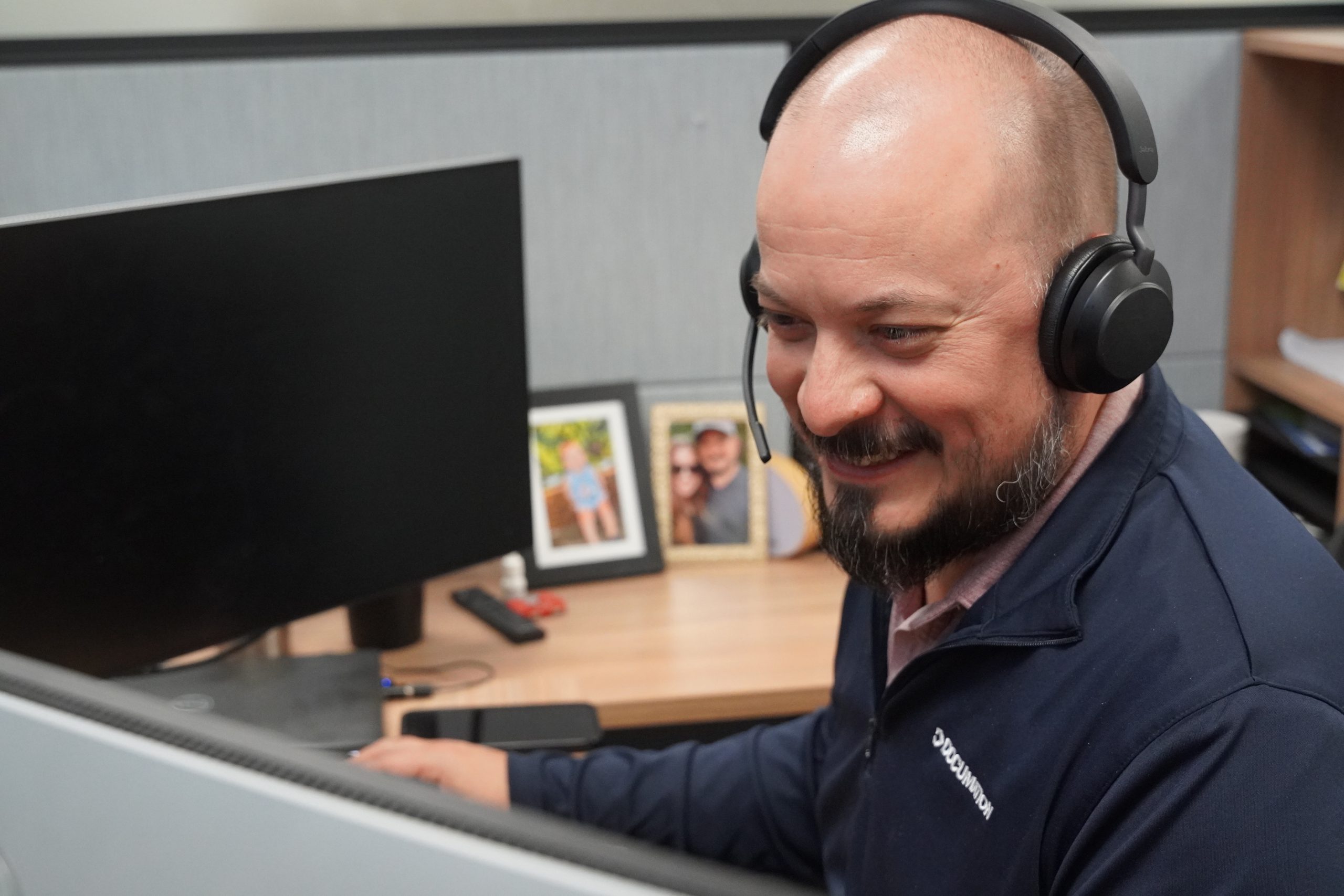 Photo of a man in a DOCUmation pullover wearing a VoIP headset, smiling at his computer