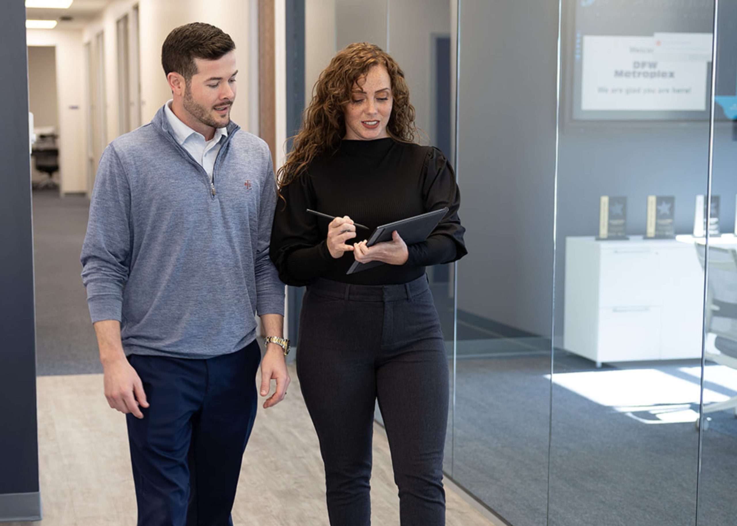 Two professionals walking and discussing work at the DOCUmation office in Dallas-Fort Worth. They are referencing a tablet and mid-conversation.