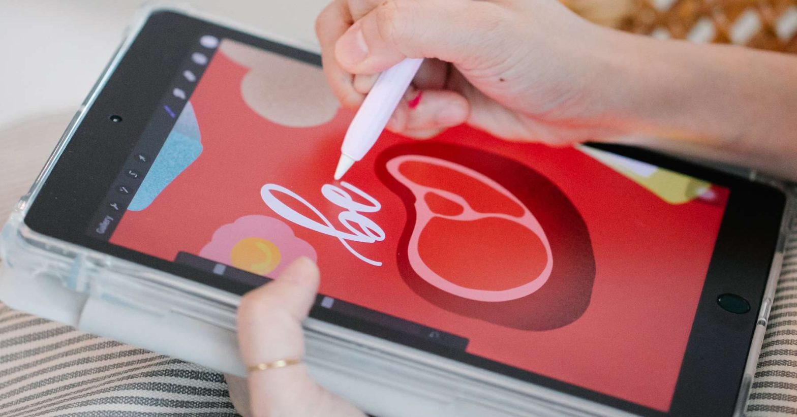 Person using a stylus to draw colorful graphic art and lettering on a tablet screen, preparing a digital design for print.