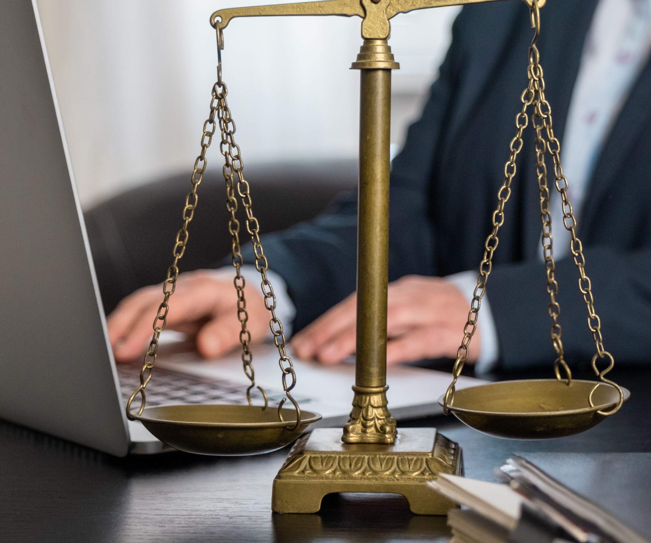 Brass balance scales positioned in front of a laptop, symbolizing the intersection of law, fairness, and digital work.