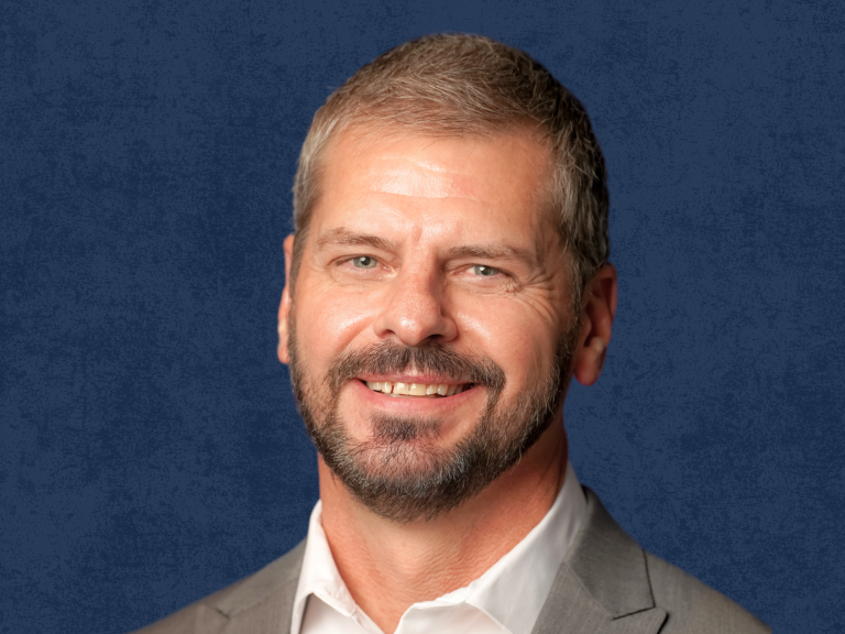 Professional headshot of a man smiling against a blue textured background.