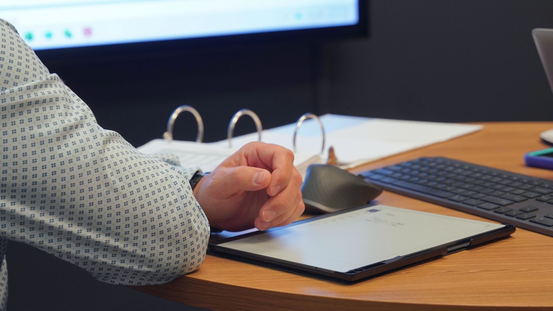 Person reviewing notes on a tablet at a desk with a keyboard and documents.