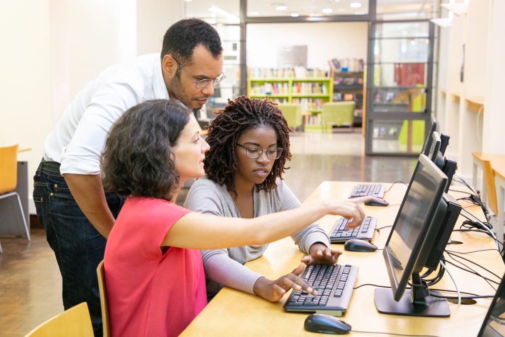 Students collaborating at desktop computers in a library computer lab environment.
