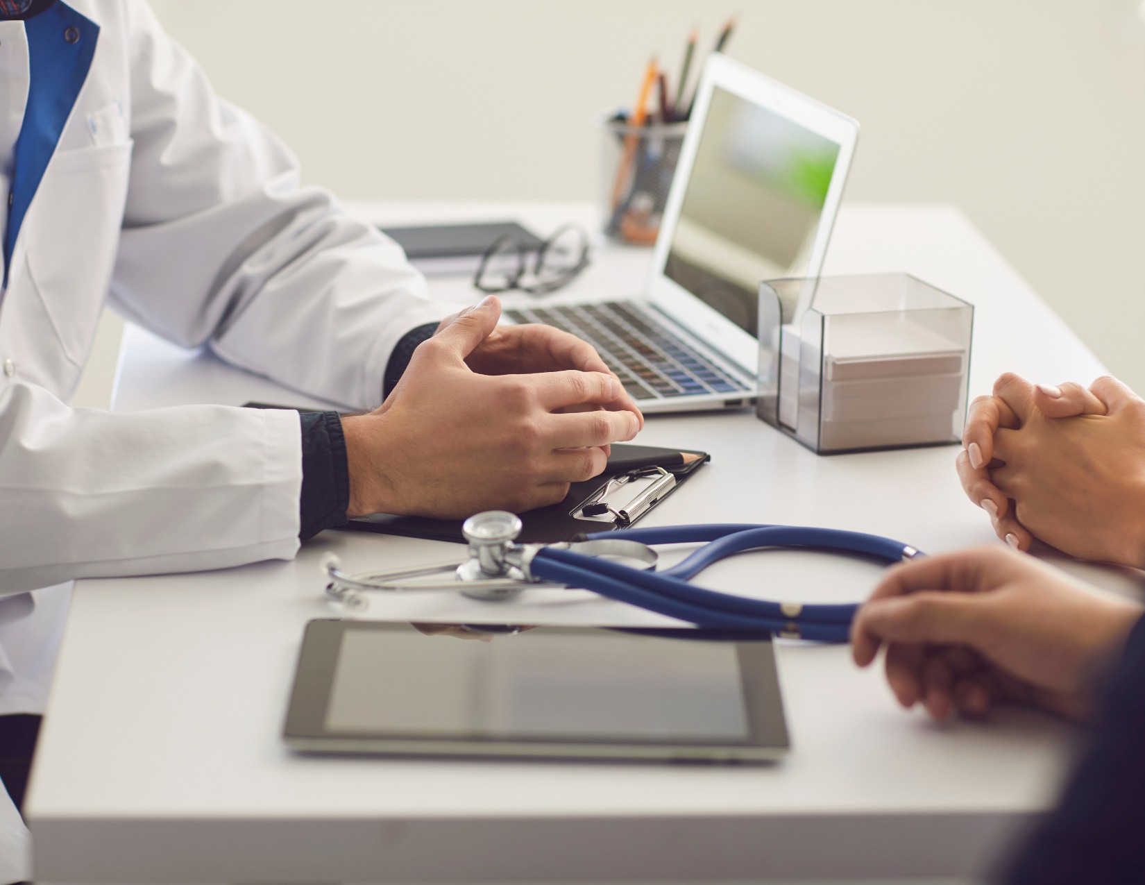 Healthcare provider consulting with a patient at a desk with a stethoscope and tablet.