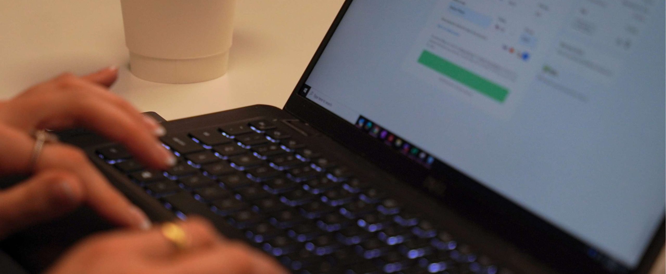 Hands typing on a laptop displaying a secure login screen, with a coffee cup on a desk in a modern office setting.
