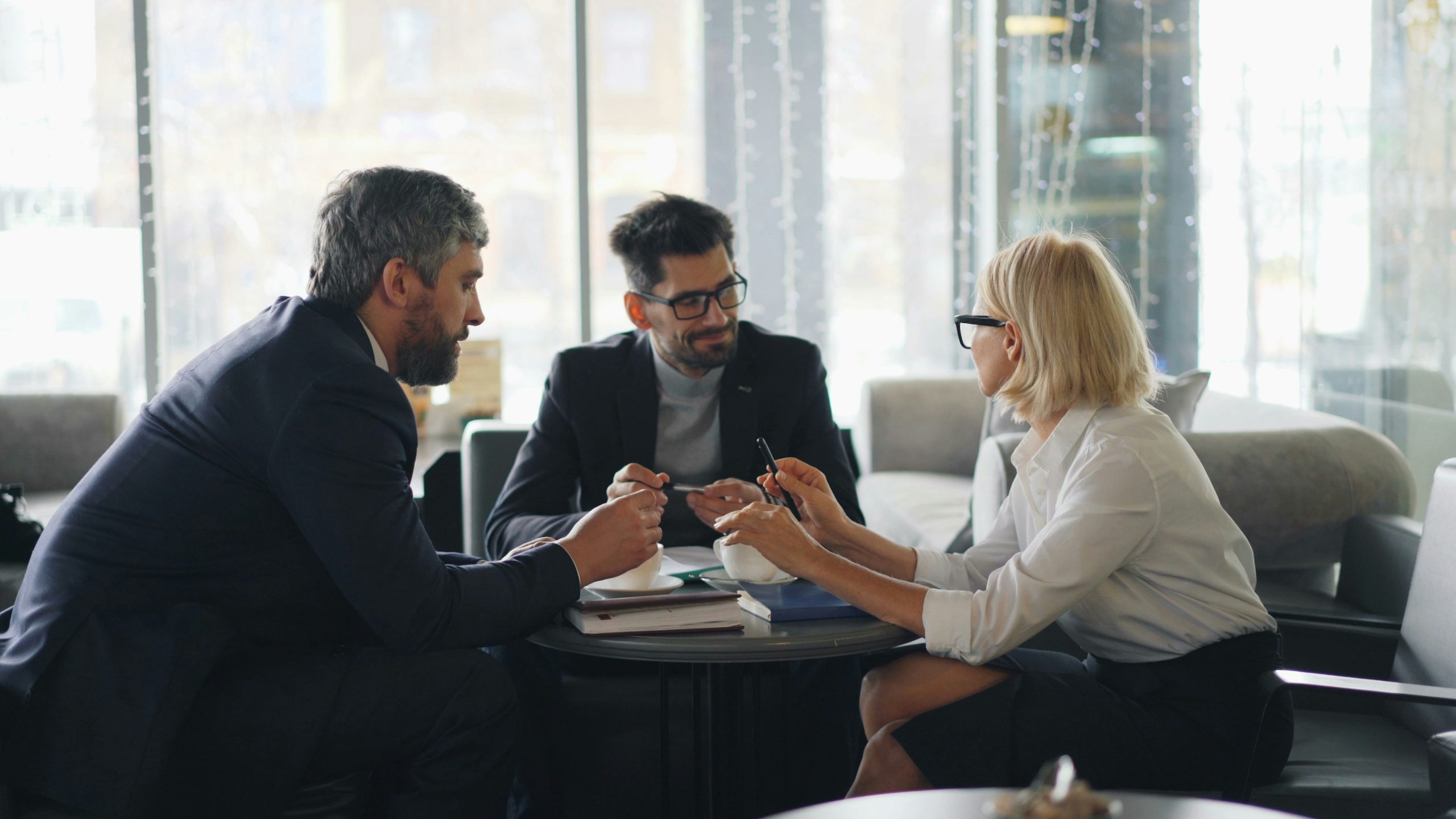 Three professionals discussing partnership over coffee in office meeting